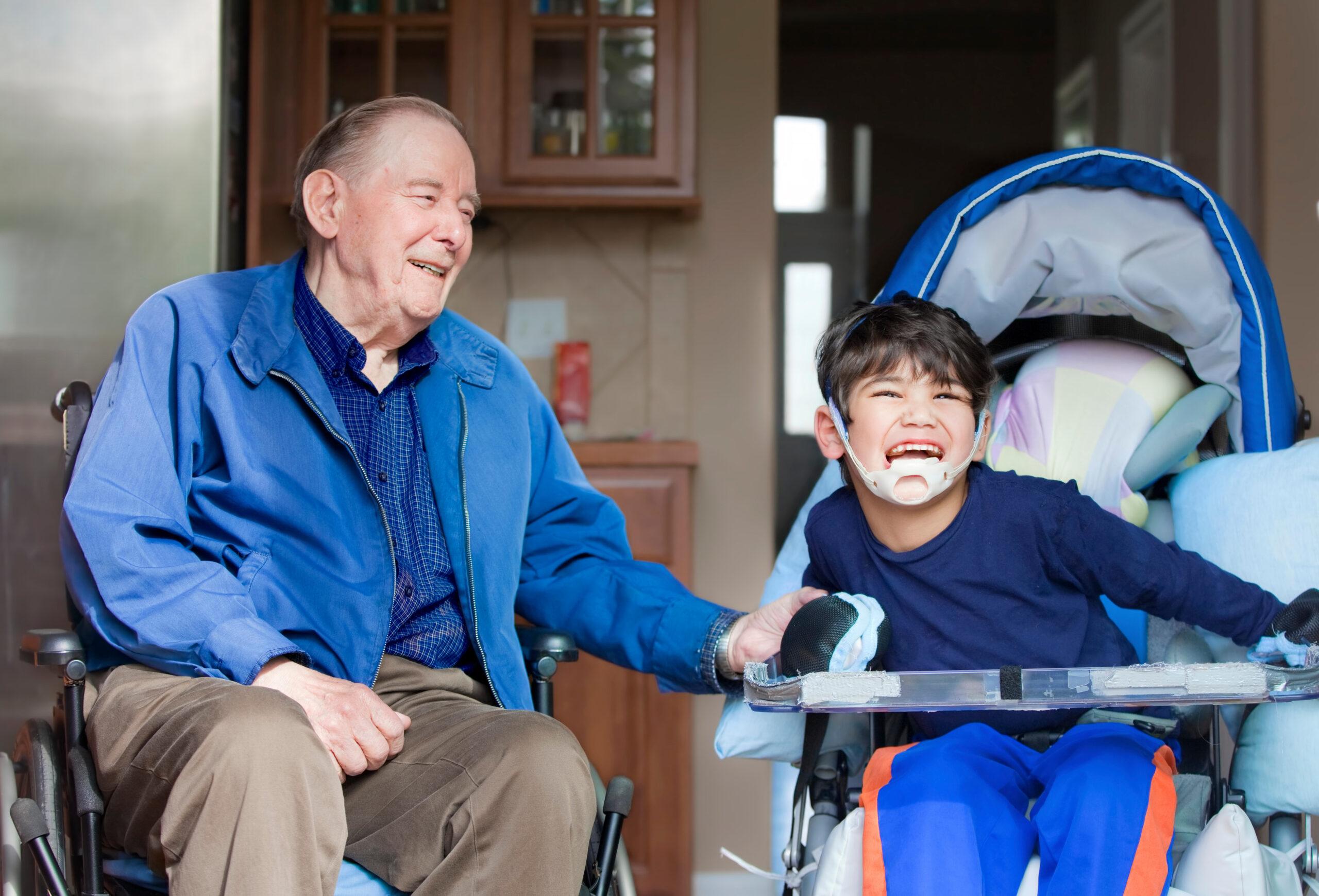 Elderly man in wheelchair laughing with disabled boy