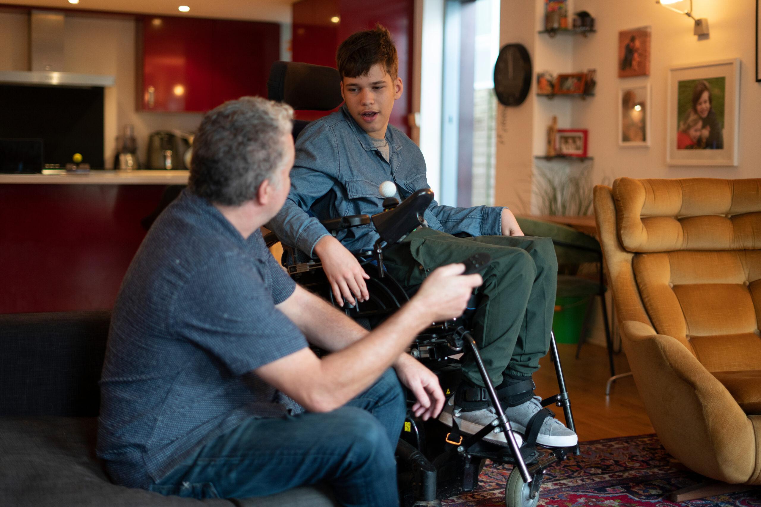 Father sitting next to son with cerebral palsy in wheelchair